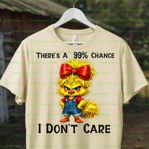 Könnte beinhalten: Beigefarbenes T-Shirt mit einem Cartoon-Küken mit roter Schleife und blauer Latzhose. Der Text auf dem Shirt lautet: "THERE'S A 99% CHANCE I DON'T CARE."