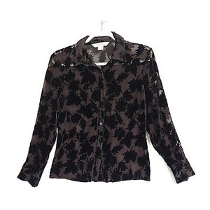 May include: A sheer, long-sleeved button-down shirt with a black leaf pattern. The shirt is a dark brown color and hangs on a white hanger against a white background. The collar and cuffs are visible.