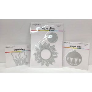 May include: Three packages of Scrapbook.com metal cutting dies. The left package contains word dies for the word JOY. The center package contains two cozy wreath shape dies. The right package contains one Christmas tree tag shape die.