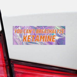 Puede incluir: Una pegatina hologr&aacute;fica con el texto "YOU CAN'T BREATHALYZE KETAMINE" en letras naranjas.