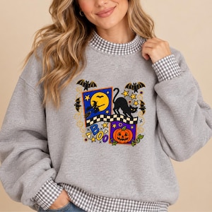 May include: A heather gray sweatshirt featuring a mock neck and cuffs with a white and gray gingham pattern. The center graphic displays a Halloween theme with a witch on a broom, a black cat, a pumpkin, bats, stars, and the word BOO.