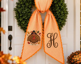 May include: A green boxwood wreath adorned with a hanging orange and white striped fabric tail featuring a scalloped edge. One side displays an embroidered turkey wearing a pilgrim hat surrounded by autumn leaves, while the other shows a large letter H.