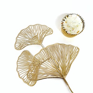 May include: Gold metal ginkgo leaf design with three leaves connected by a stem. The leaves are delicate and intricate.