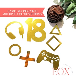 May include: Gold glitter cake toppers for an 18th birthday party. The set includes the number 18, a video game controller, headphones, a circle, a plus sign, a triangle, and a square.