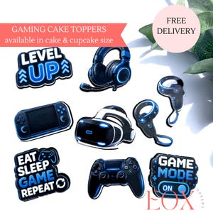 May include: A collection of gaming-themed cake toppers featuring blue and black designs. Items include a Level Up sign, headphones, a handheld console, a VR headset, two controllers, and a sign reading Eat Sleep Game Repeat and Game Mode On.
