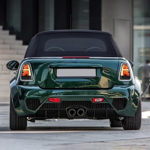 Może przedstawiać: Zielony kabriolet Mini Cooper z czarnymi kołami i czarnym zderzakiem tylnym. Samochód ma wzór Union Jack na tylnych światłach.