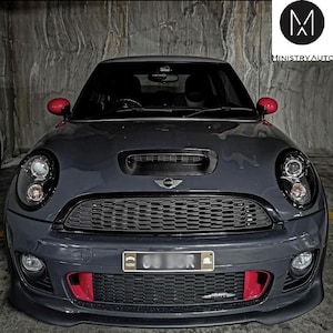 May include: A black Mini Cooper S with a black grille, red accents, and a black carbon fiber hood. The car has a black license plate with the letters "NSW" and a black and white "MINI" logo on the front.