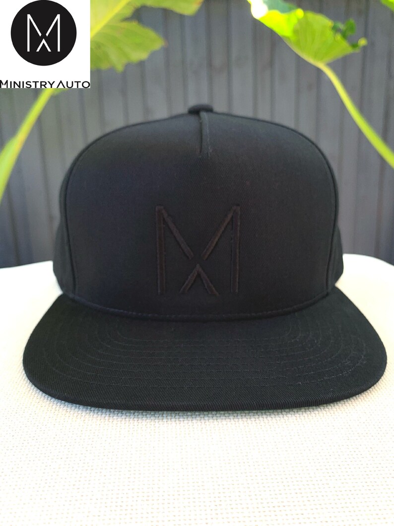 Pode incluir: Um bon&eacute; de beisebol preto de aba plana com um "M" bordado em preto na frente.