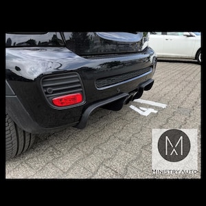Könnte beinhalten: Schwarzer Mini Cooper mit einem kundenspezifischen Heckdiffusor und doppelten Auspuffendrohren. Der Diffusor hat eine schwarze Oberfläche und ein sportliches Design. Das Auto ist auf einer befestigten Fläche geparkt. Das Bild enthält das Logo "MINISTRY AUTO".