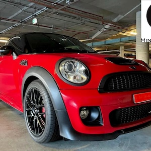 May include: A red Mini Cooper Coupe with black wheels and a black grille. The car is parked in a garage.
