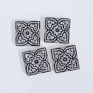 May include: Four black and white ceramic tiles with a geometric pattern. The tiles have a white background with black floral designs.