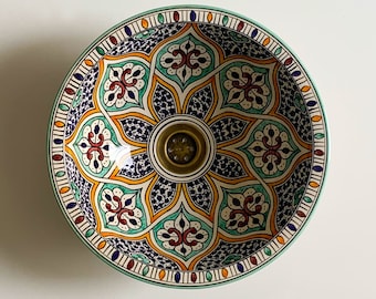 May include: A ceramic sink with a colourful Moroccan-inspired design. The sink features intricate geometric patterns in shades of blue, green, orange, and red. The sink has a brass drain.
