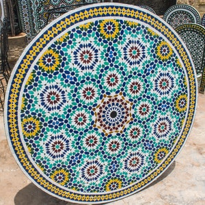Pode incluir: Uma mesa redonda de madeira com um padrão de mosaico geométrico em tons de azul, verde, amarelo e marrom. O design do mosaico apresenta formas florais e estreladas intrincadas.