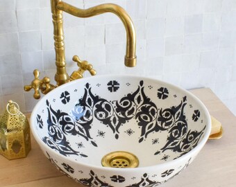Puede incluir: Un lavabo de baño de cerámica blanca con un patrón geométrico en blanco y negro. El lavabo tiene un grifo de latón con un caño curvo.