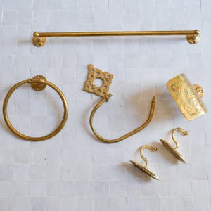Könnte beinhalten: Ein Set goldfarbener Badezimmer-Accessoires, bestehend aus einer Handtuchhalterstange, einem Handtuchring, einem Bademantelhaken, einem Toilettenpapierhalter und zwei dekorativen Haken.