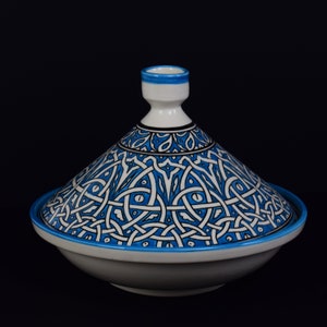 May include: A white ceramic tagine with a blue and white geometric pattern. The tagine has a domed lid and a wide base.