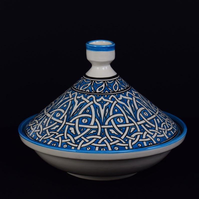 May include: A white ceramic tagine with a blue and white geometric pattern. The tagine has a domed lid and a wide base.