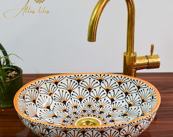May include: A white ceramic oval sink with a black and orange geometric pattern. The sink has a brass drain and is paired with a gold faucet.