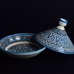 May include: A white ceramic serving dish with a blue and white geometric pattern. The dish has a matching lid with a conical shape.