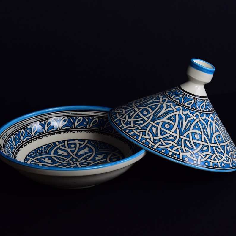 May include: A white ceramic serving dish with a blue and white geometric pattern. The dish has a matching lid with a conical shape.
