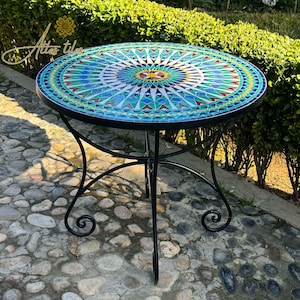 May include: A round mosaic table with a blue, green, and yellow geometric design. The table has a black metal base with a scrolled design.