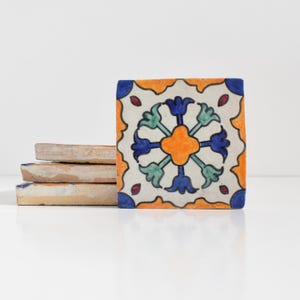 May include: Four ceramic tiles with a colorful geometric design. The tile in the front has a white background with a blue, green, and orange floral pattern.