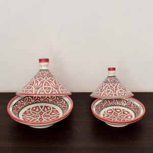 May include: Two ceramic serving dishes with lids. The dishes are white with a pink and black geometric pattern. The lids are cone-shaped and have the same pattern as the dishes.