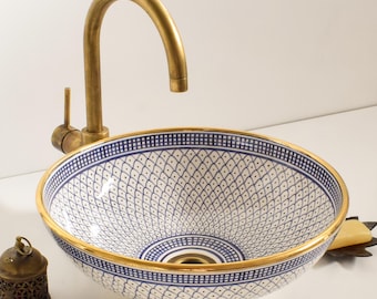Può includere: Un lavandino in ceramica bianca con un motivo geometrico blu e oro. Il lavandino ha un bordo dorato e uno scarico al centro. Un rubinetto in ottone è montato sopra il lavandino.