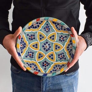 May include: A large, round ceramic plate with a colorful geometric design. The plate features a repeating pattern of blue, yellow, green, and red stars and swirls.