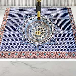 Op de afbeelding: Een blauwe en witte keramische wastafel met een geometrisch patroon. De wastafel is ingebouwd in een aanrechtblad met een decoratieve rand.