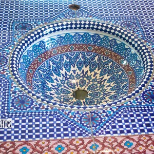 Op de afbeelding: Een blauwe en witte keramische gootsteen met ingewikkelde geometrische patronen. De gootsteen is in een betegelde oppervlakte met een vergelijkbaar patroon geplaatst. De tekst "Atlas Tiles" is zichtbaar in de linkerbenedenhoek van de afbeelding.