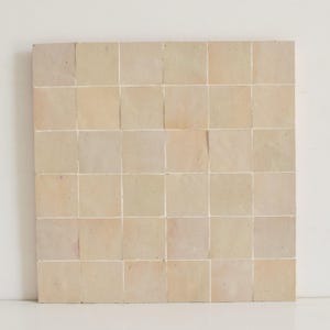 Puede incluir: Una hoja de azulejos marroquíes beige con un sutil tono rosado. Los azulejos están dispuestos en una cuadrícula y tienen una superficie ligeramente texturizada.