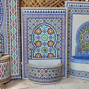 May include: A Moroccan-style tiled fountain with a blue, green, yellow, and white geometric pattern. The fountain has a curved basin and a traditional archway design.