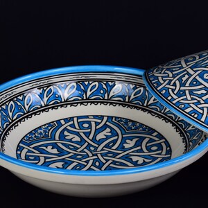 May include: A white ceramic bowl with a blue and black geometric pattern. The bowl has a matching lid.
