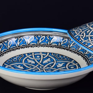 May include: A white ceramic bowl with a blue and black geometric pattern. The bowl has a matching lid.
