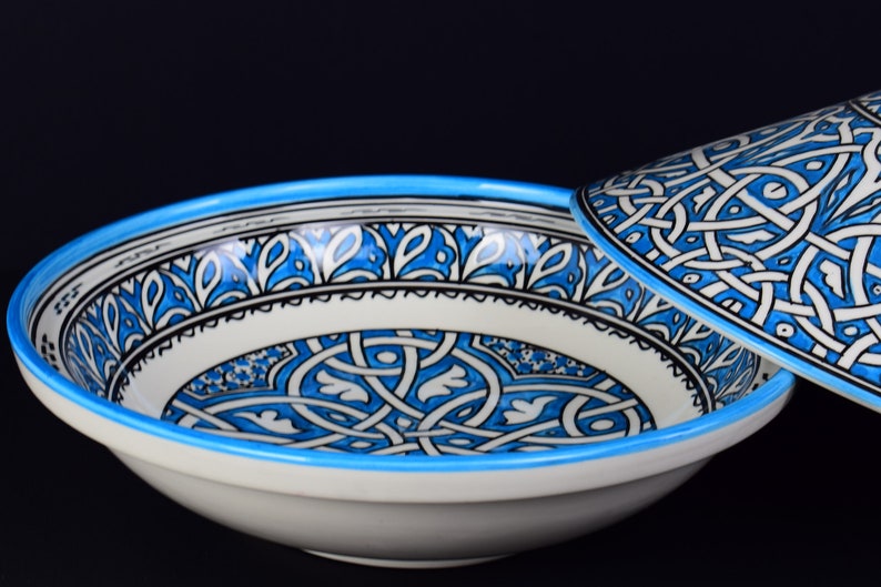 May include: A white ceramic bowl with a blue and black geometric pattern. The bowl has a matching lid.