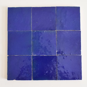 May include: Nine square, deep blue tiles arranged in a grid. The tiles have a glossy finish and are slightly irregular in shape, suggesting a handmade quality. The cobalt blue colour is consistent across all tiles, creating a cohesive look.