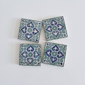 May include: Four square ceramic tiles with a blue and green geometric pattern. The tiles have a white background and feature a repeating design of stylized flowers and leaves.