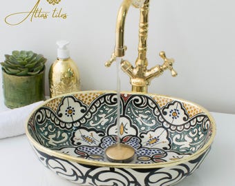 May include: Oval ceramic sink with intricate floral and geometric patterns in shades of green, blue, yellow, and red. The sink has a gold rim and is paired with a gold faucet.