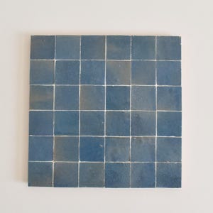 Könnte beinhalten: Eine Fliese aus blauen Keramikfliesen, die in einem Raster angeordnet sind. Jede Fliese hat einen leicht anderen Blauton, was eine subtile Farbvariation erzeugt.