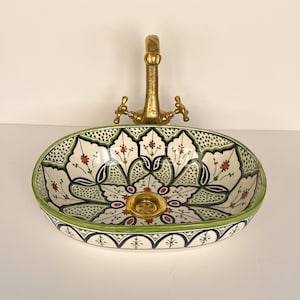 May include: Oval ceramic sink with a green and white floral design. The sink has a gold-coloured drain and a brass faucet.
