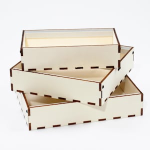 Può includere: Tre scatole di legno impilate l'una sull'altra. Le scatole sono in legno chiaro con una finitura naturale e hanno un bordo marrone attorno ai bordi. Le scatole sono vuote.