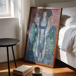 May include: A framed rectangular art print featuring a portrait of a person wearing a wide-brimmed black hat, a high-collared white garment, and a long blue scarf. The artwork displays a vibrant background with pink, green, and blue floral patterns.
