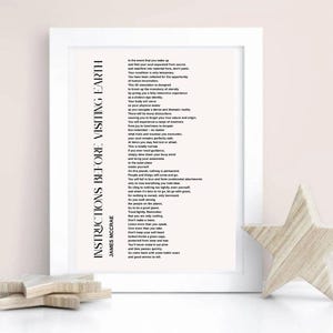 May include: A white framed print featuring the poem Instructions Before Visiting Earth by James McCrae in black text on a light background. The vertical title is printed on the left side, with the body text aligned to the right.