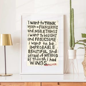 May include: A framed wall art print featuring black hand-lettered text on a cream background. The text reads: I WANT TO THINK AGAIN OF DANGEROUS AND NOBLE THINGS I WANT TO BE LIGHT AND FROLICSOME I WANT TO BE IMPROBABLE BEAUTIFUL AND AFRAID OF NOTHING AS THOUGH I HAD WINGS. The name MARY OLIVER is printed in red at the bottom.