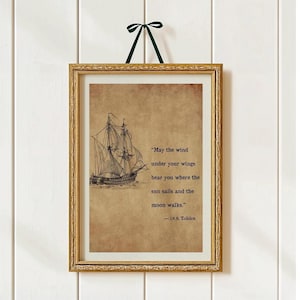 May include: Framed print featuring a vintage-style illustration of a sailing ship. The artwork includes a quote by J.R.R. Tolkien: "May the wind under your wings bear you where the sun sails and the moon walks." The frame is gold, and the print is hung with a green ribbon.