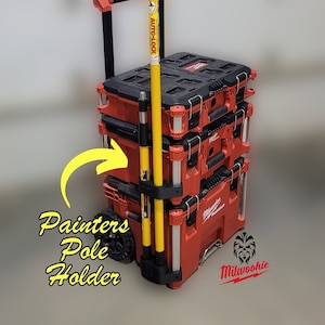 May include: A red and black rolling toolbox with a yellow painters pole holder. The toolbox has the text "Milwaukee" on the side. The toolbox is on a grey surface.