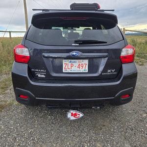 K&ouml;nnte beinhalten: Ein schwarzer Subaru XV Crosstrek mit einem Nummernschild "ZLP-497" und einem Kansas City Chiefs-Logo an der Anh&auml;ngerkupplung. Das Auto hat ein Dachgep&auml;cktr&auml;ger mit einer schwarzen Box auf dem Dach.