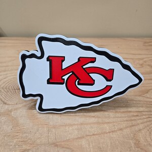 K&ouml;nnte beinhalten: Ein wei&szlig;er und schwarzer 3D-gedruckter Pfeilspitz mit einem roten "KC"-Logo im Inneren. Der Pfeilspitz ist ein beliebtes Symbol f&uuml;r die Kansas City Chiefs.