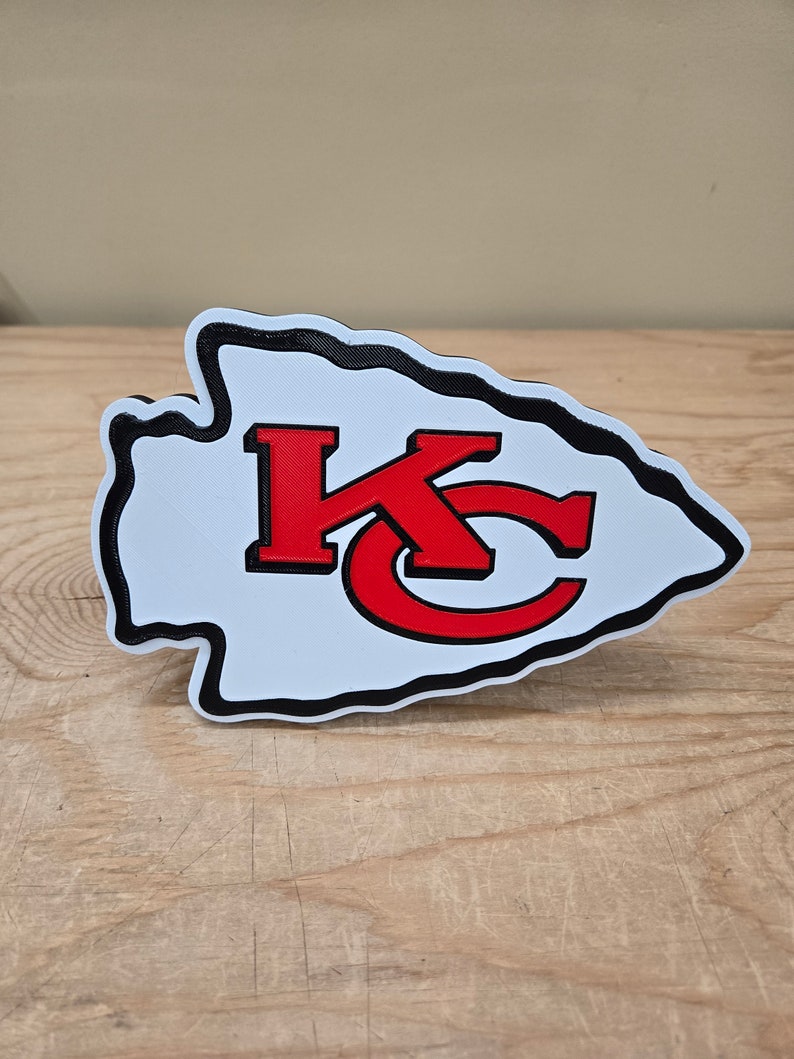 K&ouml;nnte beinhalten: Ein wei&szlig;er und schwarzer 3D-gedruckter Pfeilspitz mit einem roten "KC"-Logo im Inneren. Der Pfeilspitz ist ein beliebtes Symbol f&uuml;r die Kansas City Chiefs.